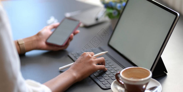 在办公室使用空白屏幕智能手机同时在数字平板电脑上打字的年轻女商业女青图片