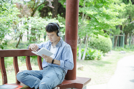 帅气大学生坐在凉亭听音乐看书