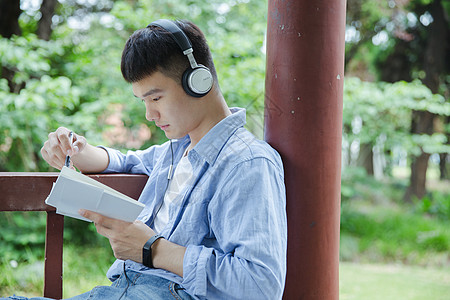 帅气大学生坐在凉亭听音乐看书背景图片
