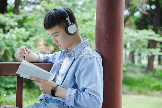 帅气大学生坐在凉亭听音乐看书