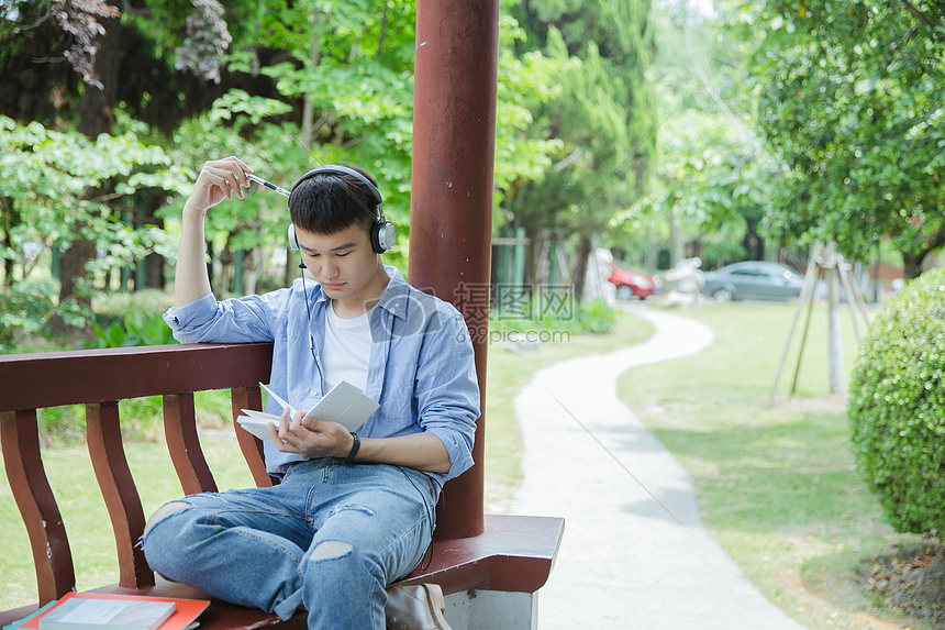 帅气大学生坐在凉亭听音乐看书