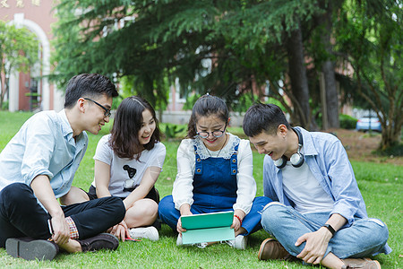 插耳机平板电脑男女大学生们坐草地上聊天休息背景