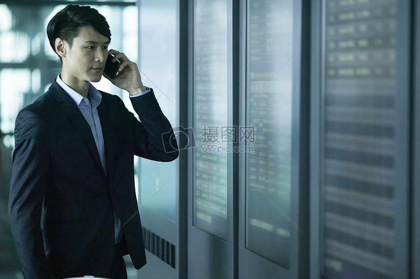 商务男士在机场时间表前用手机通话图片