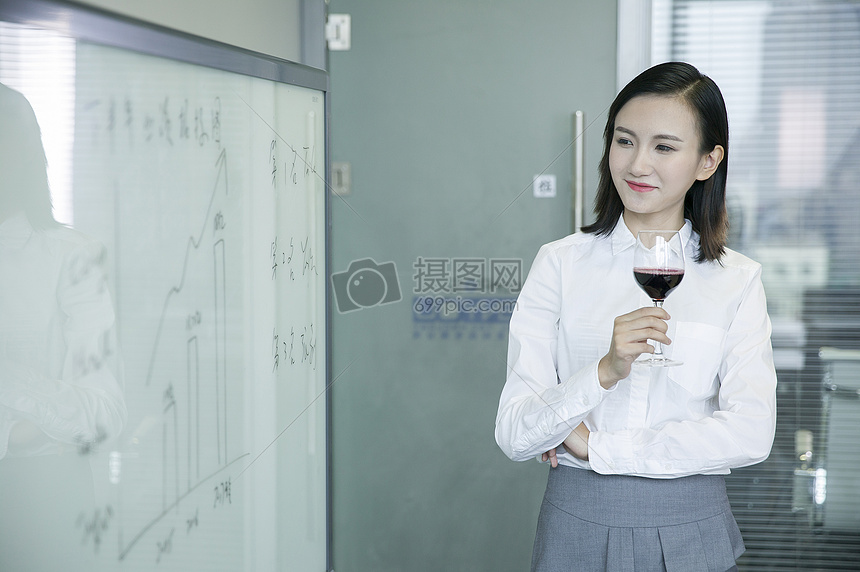 商务女士手举红酒看着会议板上数据图片