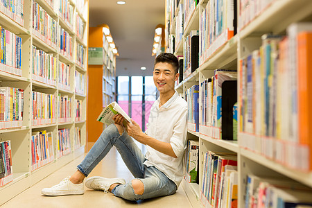 坐在图书馆书架旁看书的男生图片
