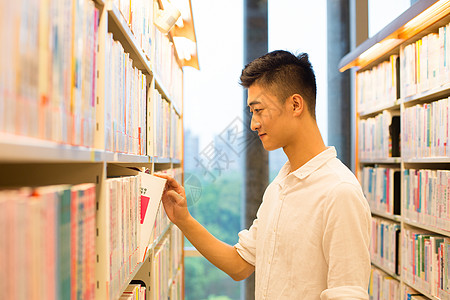 高中生学习男生在图书馆书架旁选看图书背景