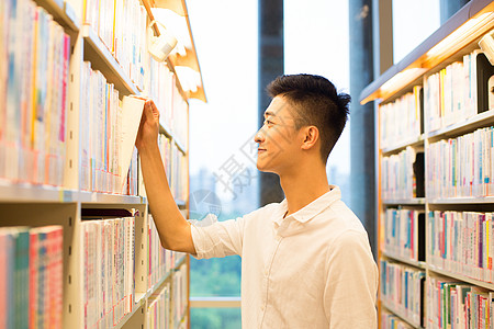 男生在图书馆书架旁选看图书背景