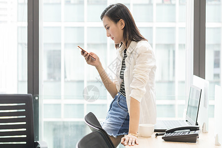 坐着使用手机的办公室女职员背景图片