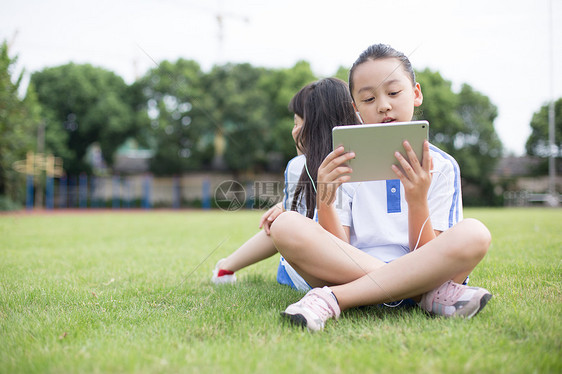 坐在草坪上使用平板电脑的小学生图片