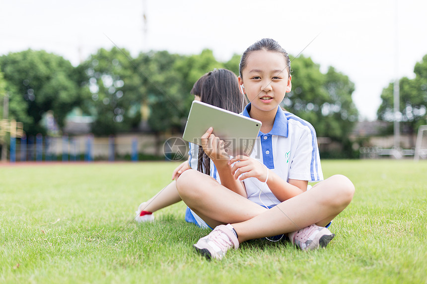 坐在草坪上使用平板电脑的小学生图片