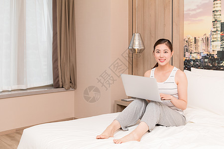 坐在床上玩电脑休闲放松的年轻女性高清图片