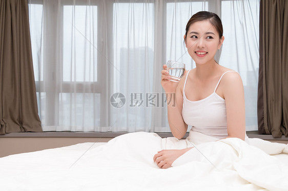 早起睡前坐在床上喝水的美女图片
