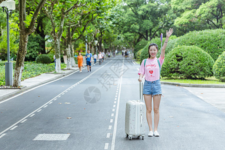 校园内女生拉旅行箱挥手高清图片