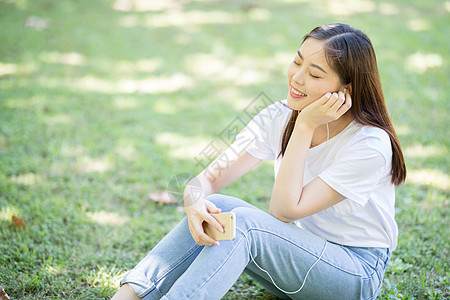 校园草坪上看手机听音乐的女生背景