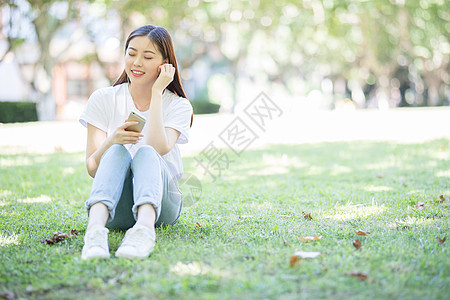 校园草坪上看手机听音乐的女生图片