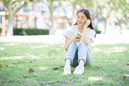 校园草坪上看手机听音乐的女生高清图片