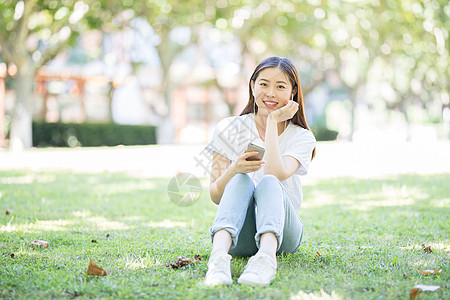 校园草坪上看手机听音乐的女生图片