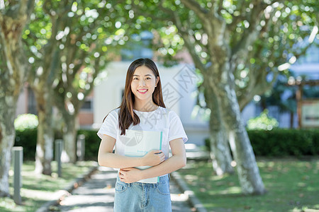 女大学生抱书图走在校园林荫道下的甜美女生背景