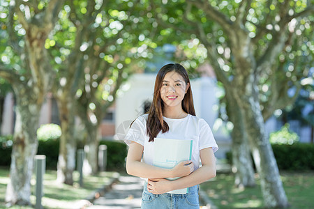 女大学生抱书图走在校园林荫道下的甜美女生背景