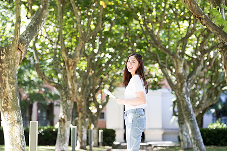 女大学生抱书图走在校园林荫道下的甜美女生背景