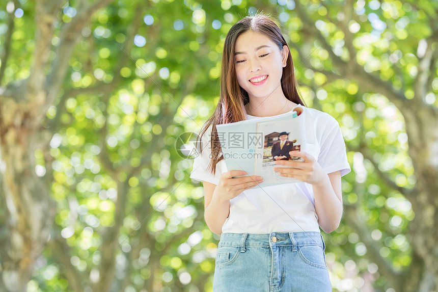 校园林荫道上微笑看书的学生图片