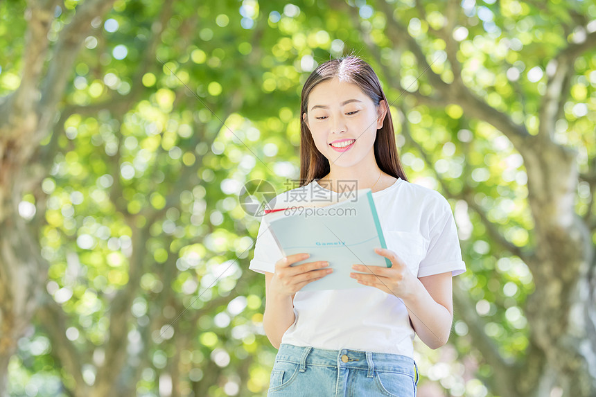 校园林荫道上微笑看书的学生图片