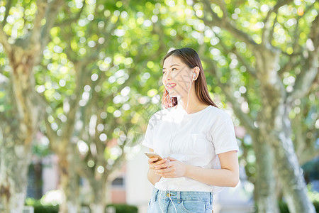 大学生手机树下用手机听音乐的甜美女生背景