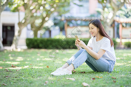 学生听音乐坐在校园草坪上玩手机的女生背景