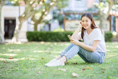 女大学生听音乐坐在校园草坪上玩手机的女生背景