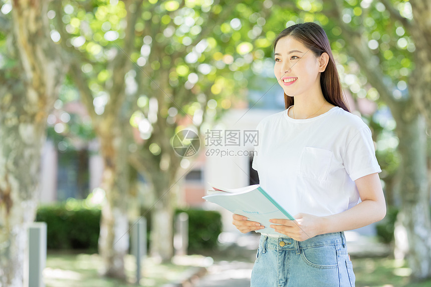 校园林荫道上微笑看书的学生图片