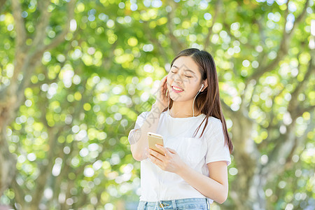 树林下戴耳机听音乐的甜美女生背景图片