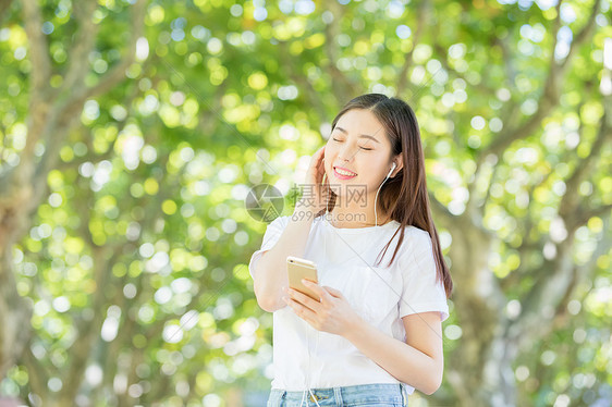 树林下戴耳机听音乐的甜美女生图片