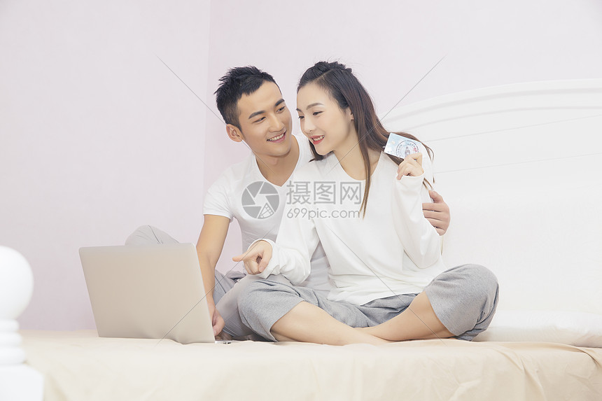 年轻夫妇在卧室用电脑购物图片