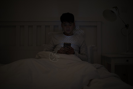 睡前坐在床上玩手机的男子高清图片