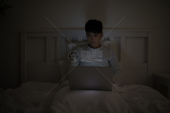 睡前坐在床上玩电脑打电脑的男子图片