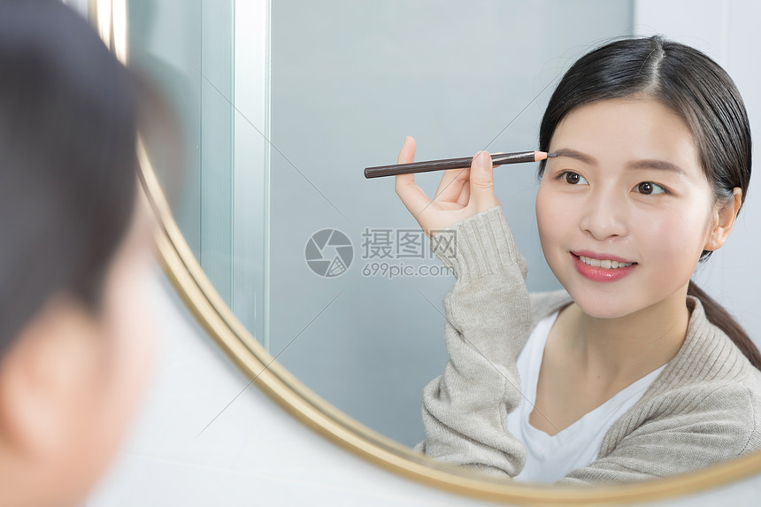 站在镜子前画眉的年轻女性图片