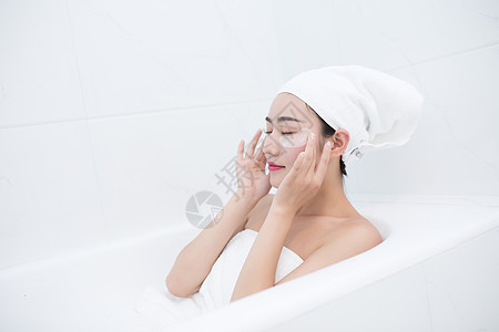 护肤模特包着头发坐在浴缸里敷眼膜的年轻美女背景