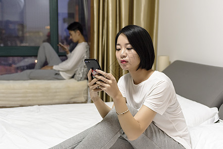 女子在床上玩手机和男子冷战背景图片