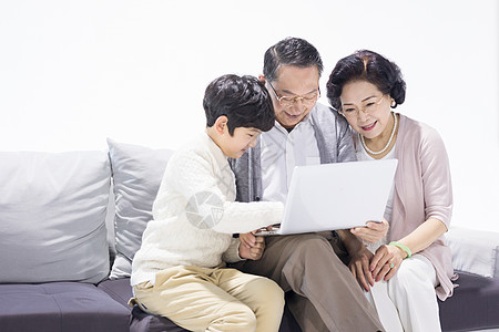 爷爷奶奶和孙子开心地坐在沙发上使用电脑图片