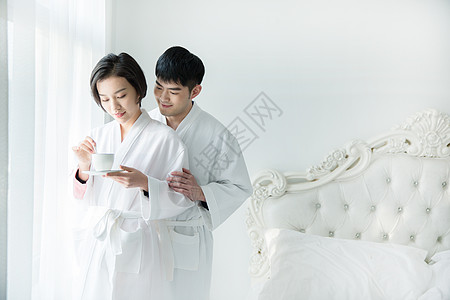 爱心情侣杯子年轻夫妇穿浴袍在卧室背景
