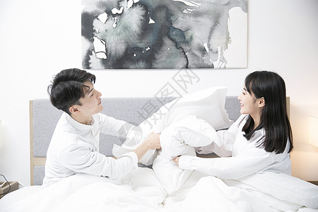 相互交谈的情侣情侣在床上用枕头相互打闹背景
