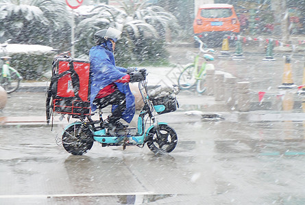 漫天飘雪寒冷冬季马路骑电动车的外卖人员背景