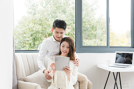 年轻夫妻幸福地坐在沙发上看平板电脑图片