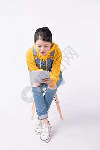 年轻女性玩平板坐在椅子上玩平板的学生背景