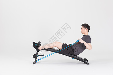 多功能仰卧板坐在运动器械上拉阻力带的健身男性背景