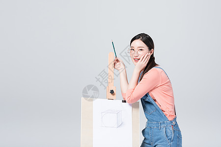 青年美女手拿铅笔站在画架旁图片