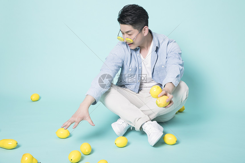 坐在地上拿着柠檬的青年男性图片