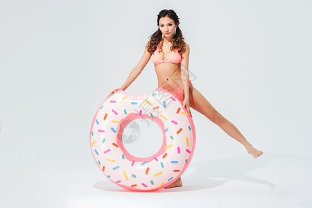 穿粉色比基尼的可爱女生拿着甜甜圈泳圈背景图片