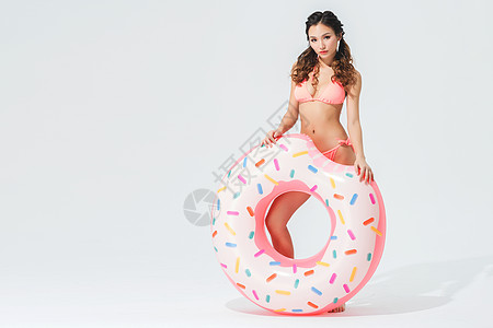 性感曲线穿粉色比基尼的可爱女生拿着甜甜圈泳圈背景