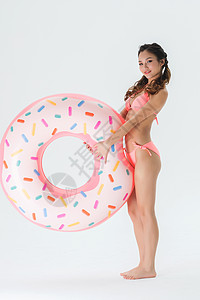 性感曲线穿粉色比基尼的可爱女生拿着甜甜圈泳圈背景
